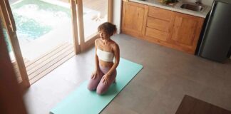 woman kneeling on yoga mat in bright kitchen near pool