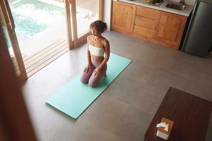 woman kneeling on yoga mat in bright kitchen near pool