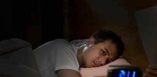 Man lying awake in bed watching an alarm clock